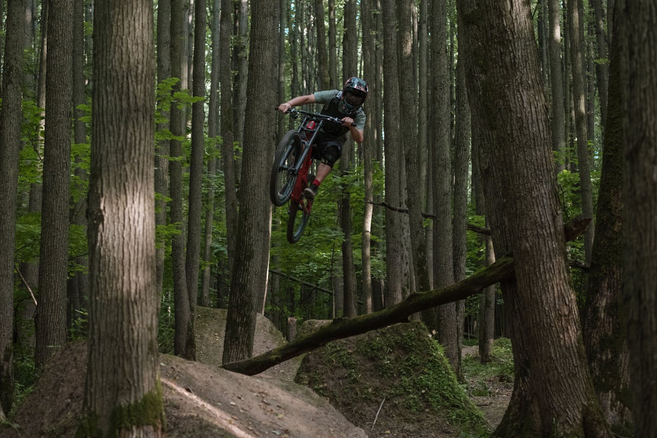 Mountain biker jumps over a trail in a dense forest, showcasing extreme sports skills.