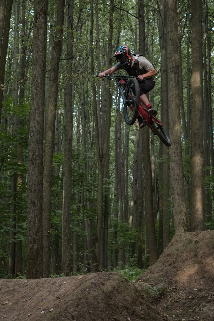 A mountain biker performing a high jump in a dense, lush forest.
